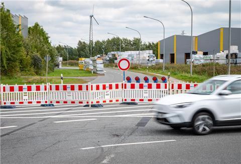 Rot-weiße Baken verhindern die Zufahrt auf eine Straße. Ein Auto fährt an der Sperrung vorbei.