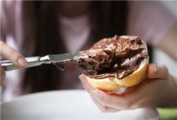 Eine Frau streicht Nuss-Nougat-Creme auf ein Brötchen. 