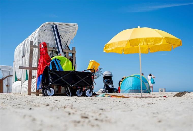 Ein Sonnenschirm steht bei sonnigem Wetter neben einem Strandkorb am Strand von Norddeich.
