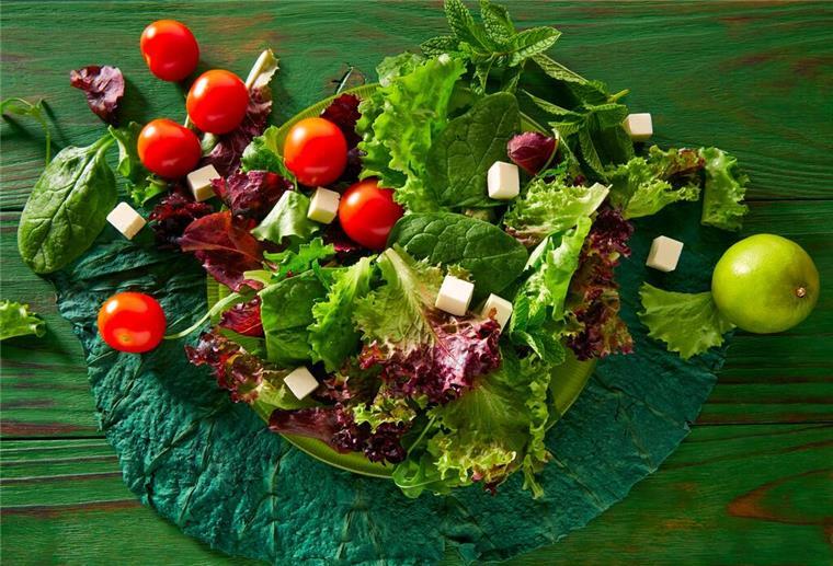 Ein grüner Salat mit Tomaten und Feta auf einem Teller. Obst und Gemüse sind gute Quellen für natürliche Vitamine, die der Körper jeden Tag braucht.