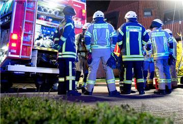  Einsatzkräfte der Feuerwehr stehen vor einem Mehrfamilienhaus, 