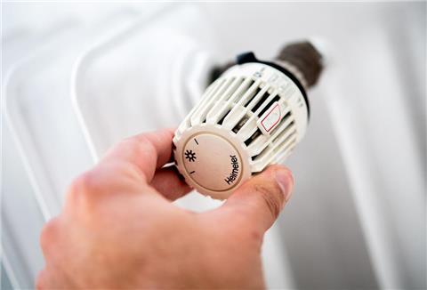 Ein Mann dreht in einer Wohnung am Thermostat einer Heizung.