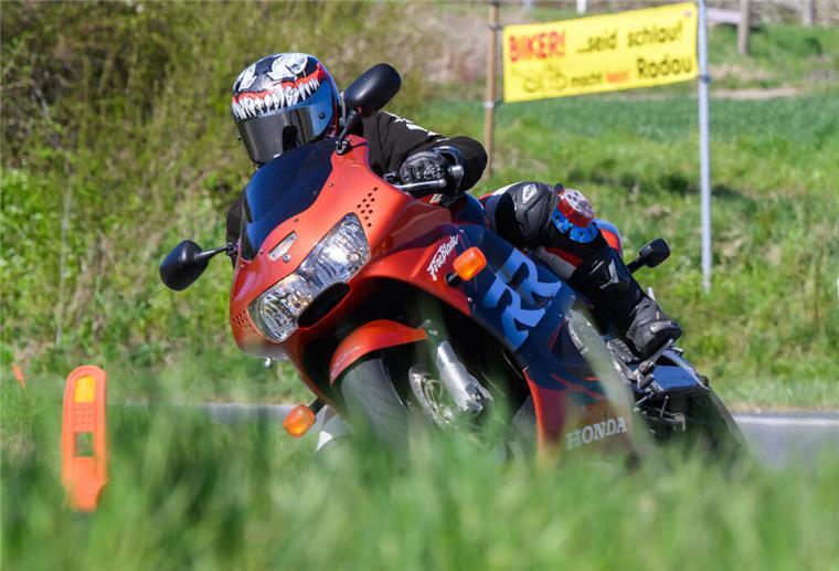 Ein Motorradfahrer fährt neben einem Banner „Biker! … seid schlau und macht kein Radau“ an einer Landstraße