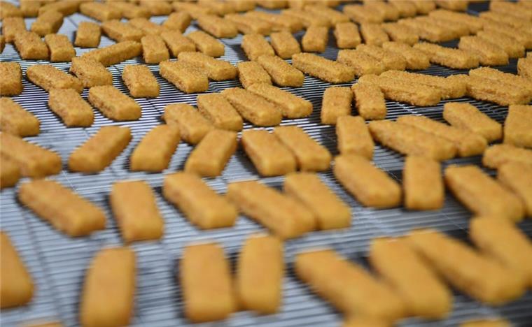 Panierte Fischstäbchen laufen in der Fischstäbchen-Produktion von Frosta in Bremerhaven über das Band.