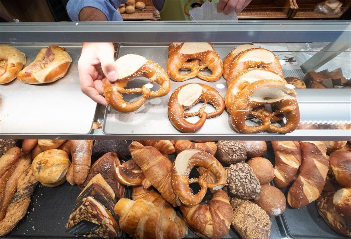 Ein Hand nimmt in einer Bäckerei eine Brezel aus einer Auslage. Ein Bäckerbesuch kann demnächst teure Folgen haben. 