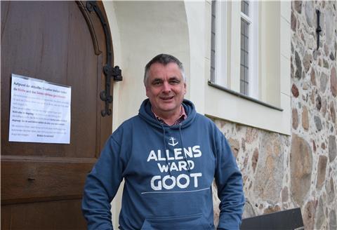 Pastor Manfred Thoden vor der geschlossenen Kirchentür in Selsingen. Trotzdem trägt er ganz bewusst den Hoodie mit dem plattdeutschen Spruch „Allens ward Goot“ - alles wird gut.