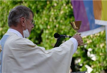 Pfarrer Ulrich Hinzen hält bei einem Open-Air-Segnungsgottesdienst für Liebende vor der Kirche Christi Auferstehung in Köln einen Kelch. Im Hintergrund ist eine Regenbogenfahne zu sehen.
