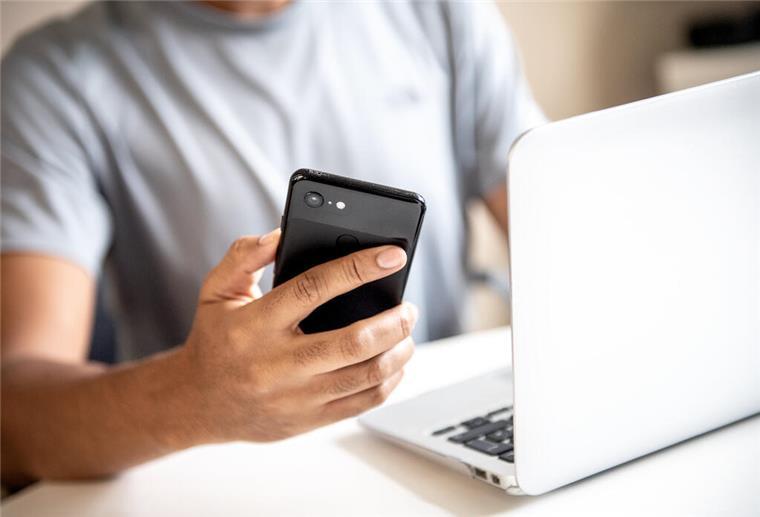 Phishing-Gefahr: Betrügerische E-Mails erkenne und vermeiden Ein Mann hält ein Handy in der Hand und sitzt vor dem Laptop