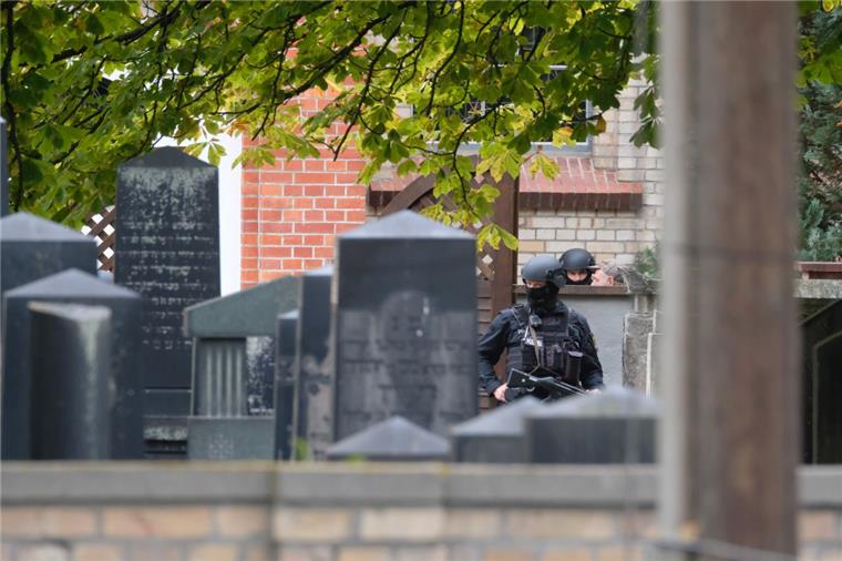 Polizisten mit Schutzhelmen stehen zwischen Grabsteinen auf dem jüdischen Friedhof in Halle. 