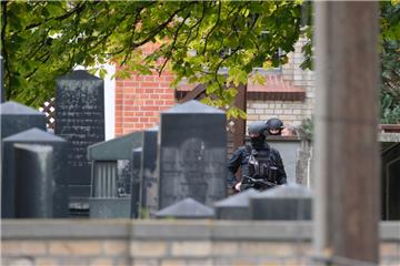 Polizisten mit Schutzhelmen stehen zwischen Grabsteinen auf dem jüdischen Friedhof in Halle. 