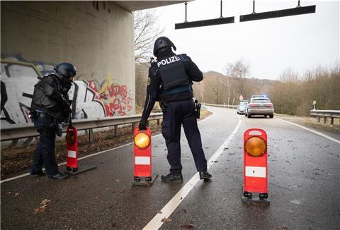 Polizeibeamte stehen an einer Absperrung an der Kreisstraße 22 rund einen Kilometer von dem Tatort, an dem zwei Polizeibeamte durch Schüsse getötet wurden.