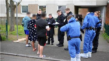 Polizisten, zum Teil in Schutzkleidung, kontrollieren Anwohner vor einem Wohnkomplex.
