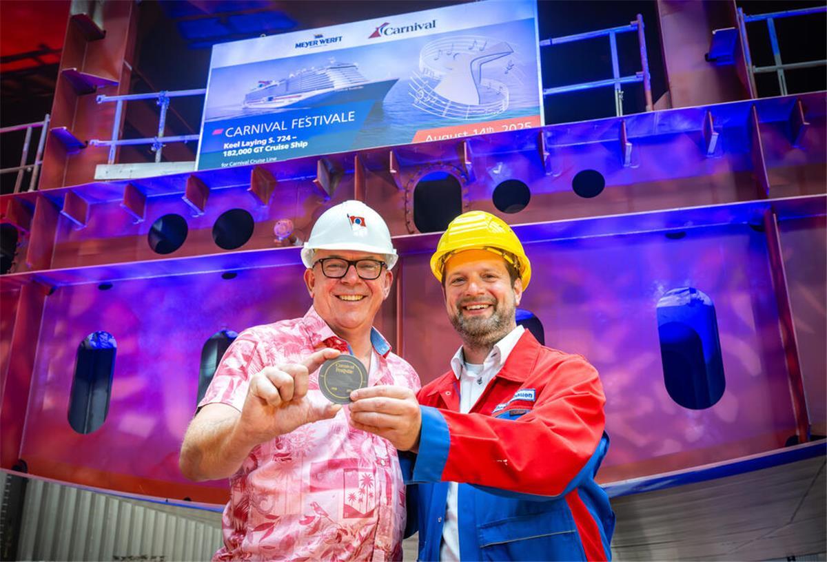 Meyer Werft legt neues Kreuzfahrtschiff für Carnival Cruise Line auf Kiel Zwei Männer in Schutzhelmen und Arbeitskleidung halten bei der Kiellegung der „Carnival Festivale“ eine Gedenkmedaille in den Händen. Im Hintergrund ist ein Schiffsrumpf mit einem Bildschirm zu sehen, der den Namen des Kreuzfahrtschiffes anzeigt.
