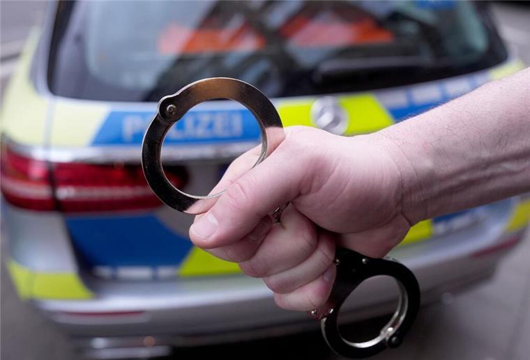 Nach Zellen-Nacht: 57-Jähriger rastet aus – und wird direkt wieder festgenommen Ein Polizist hält Handschellen vor einem Einsatzfahrzeug hoch.