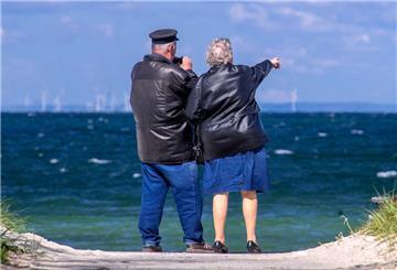 Ein Rentnerpaar steht am ansonsten menschenleeren Strand und schaut aufs Meer.