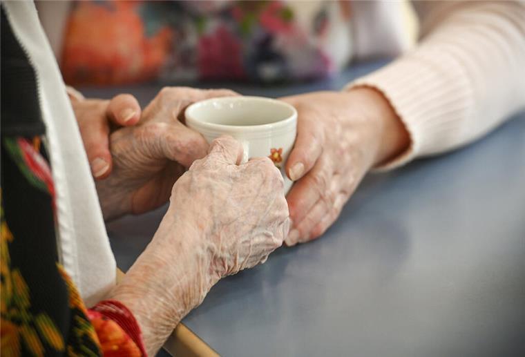 Eine Betreuungskraft hilft einer blinden Frau mit der Kaffeetasse