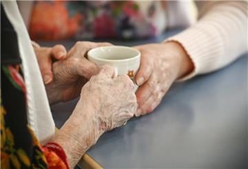Eine Betreuungskraft hilft einer blinden Frau mit der Kaffeetasse