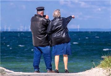 Ein Rentnerpaar steht am ansonsten menschenleeren Strand und schaut aufs Meer.