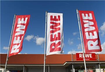 Drei Fahnen mit der Aufschrift Rewe hängen vor einem Rewe-Markt. 