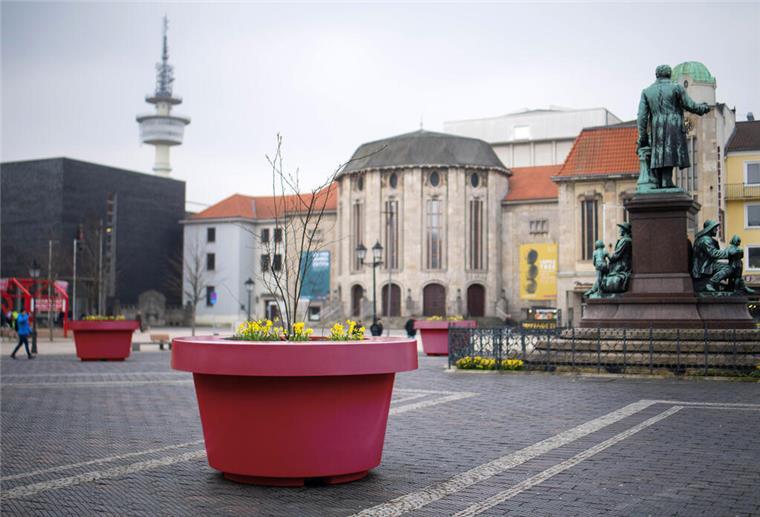 Ein weinroter Kübel ist auf einem öffentlichen Platz zu sehen.