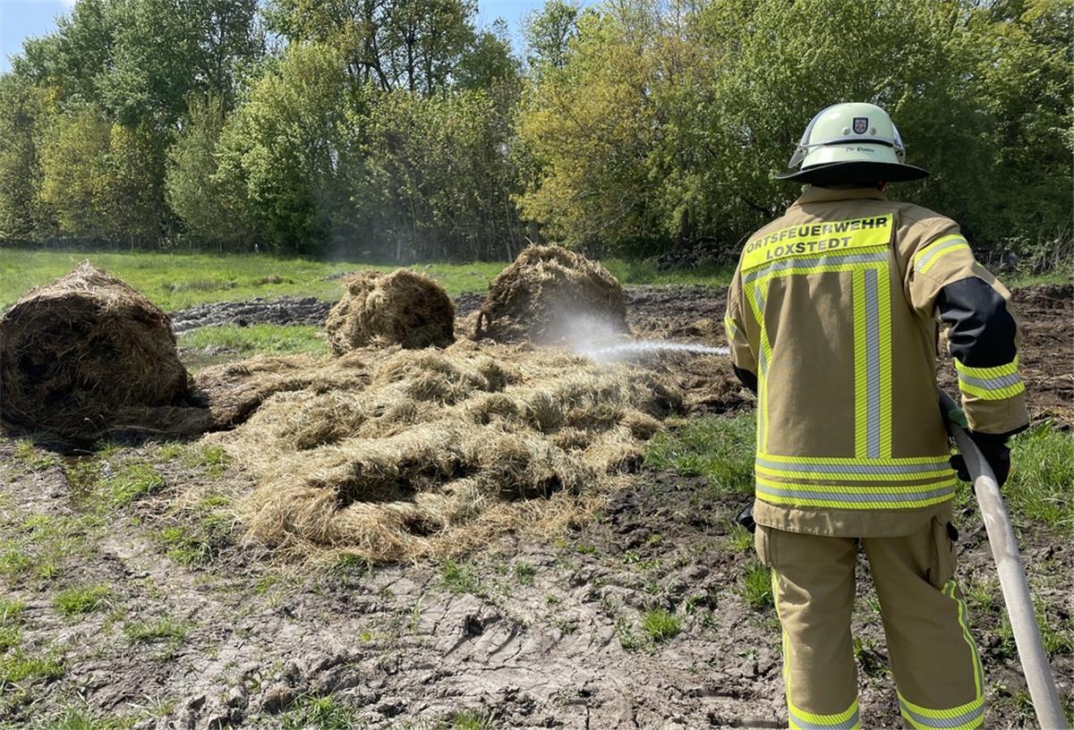 Ein Feuerwehrmann löscht brennende Strohballen.