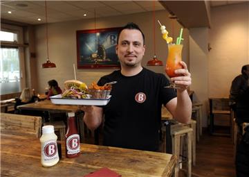 Sam Aypar ist der Betriebsleiter der Burger Bar am Theodor-Heuss-Platz. In der Hand hält er ein Hamburger-Gedeck mit Süßkartoffel-Pommes und einen der Cocktails, die die Bar ihren Besuchern anbietet.