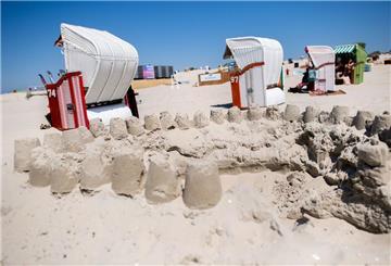 Zahlreiche Strandkörbe stehen bei sonnigem Wetter hinter einer Sandburg am Strand der Insel Borkum.