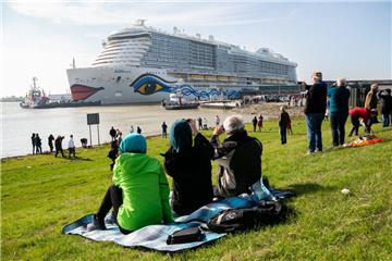 Schaulustige sind auf einem Deich und beobachten, wie das Kreuzfahrtschiff "AIDAnova" während der Überführung auf der Ems von Schleppern durch das Ems-Sperrwerk Gandersum manövriert wird.