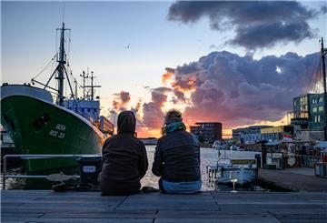 Menschen schauen am Fischereihafen auf den Sonnenuntergang.