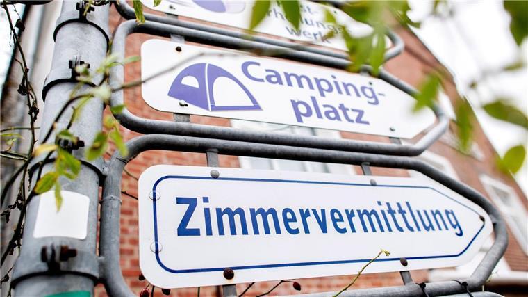 Schilder mit den Aufschriften „Campingplatz“ und „Zimmervermittlung“ hängen an einer Kreuzung.