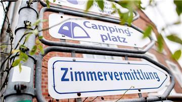 Schilder mit den Aufschriften „Campingplatz“ und „Zimmervermittlung“ hängen an einer Kreuzung.