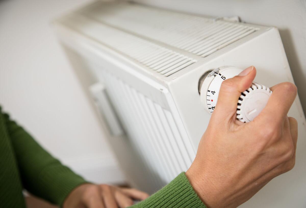 Eine Frau dreht eine Heizung auf. 