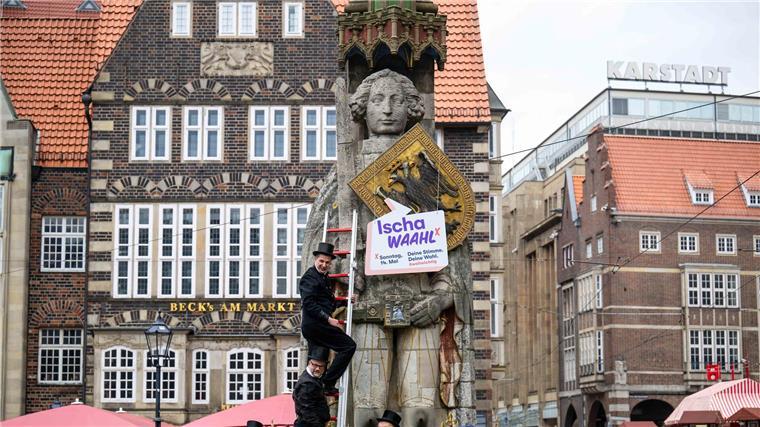 Schornsteinfeger hängen ein Schild mit der Aufschrift „Ischa Waahl!“ an den Bremer Roland.