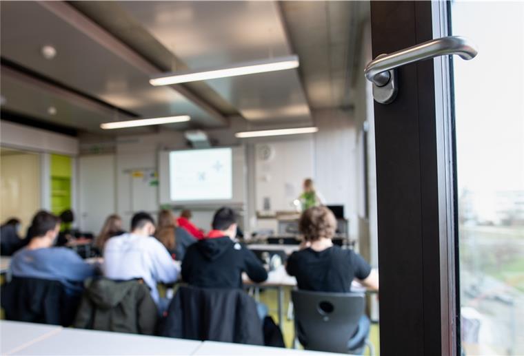 Schülerinnen und Schüler nehmen mit Mund- und Nasenschutz am Unterricht teil. Im Vordergrund ist ein geöffnetes Fenster zu sehen.