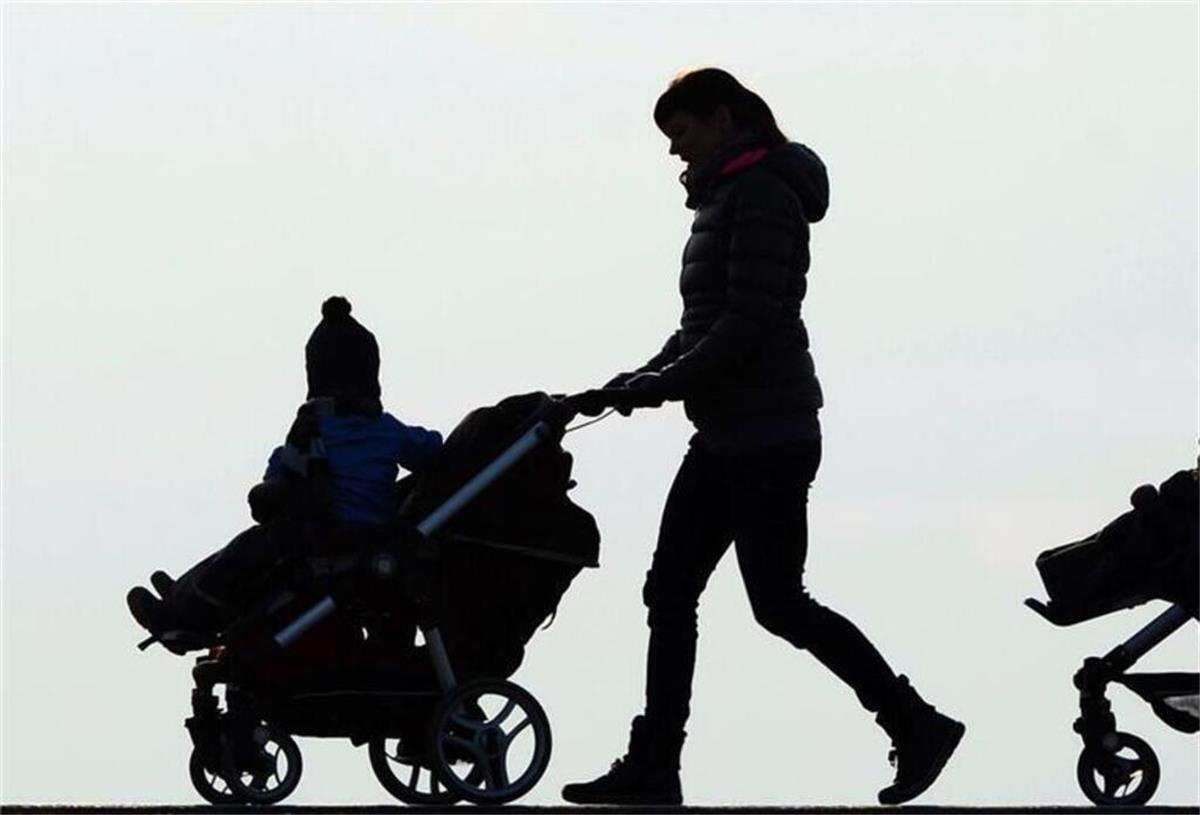 Bis zu 100 Euro mehr: Dieser Extra-Zuschuss für Eltern bringt Geld aufs Konto Eine Mutter schiebt ihren Kinderwagen eine Landstraße entlang.