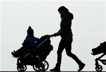 Eine Mutter schiebt ihren Kinderwagen eine Landstraße entlang.