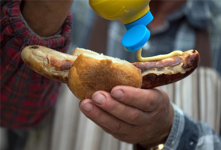 Senf auf einer Thüringer Rostbratwurst in der Hand eines Mannes.