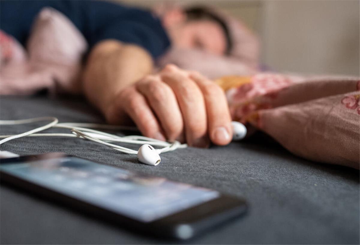 Zwischen Trance und Träumen: Ausstellung zum Schlaf Ein Mann schläft mit einem Smartphone neben sich.