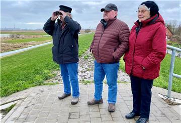 Ein Mann mit Fernglas, ein Mann mit roter Jacke und eine Frau mit roter Jacke stehen auf dem Deich und blicken in die Ferne.