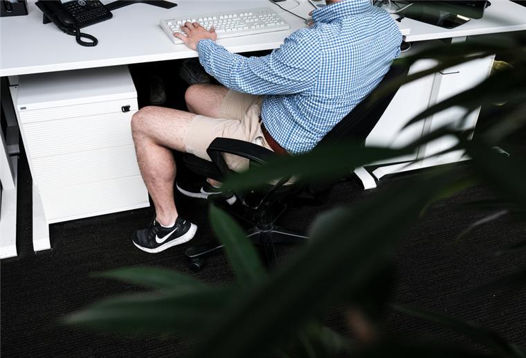 Ein Mann sitzt mit kurzer Hose an seinem Arbeitsplatz.