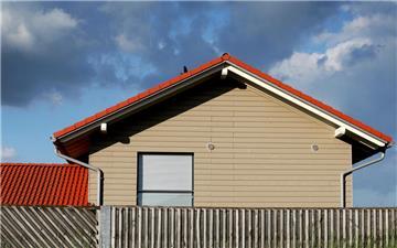 Hinter einem Zaun ist ein Haus zu sehen, das Dach ist rot. Die Hauspreise im Kreis Cuxhaven sinken.