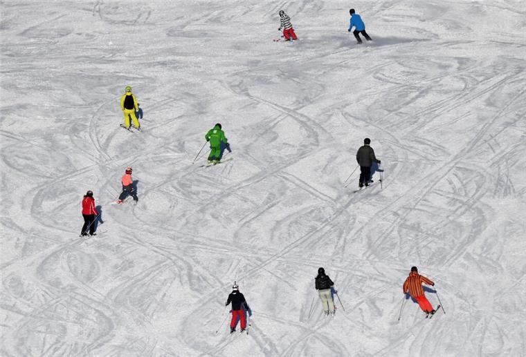Skifahrer fahren bei Sonnenschein auf einer Skipiste.
