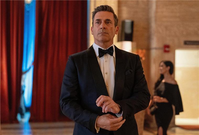 Ein Mann im Anzug (mit Fliege) guckt ernst. Unscharf im Hintergrund ist eine Frau in einem dunklen Kleid zu sehen. Smart und stinkreich: Hedgefonds-Manager Andrew (Jon Hamm) verliert in der Serie „Your Friends and Neighbors“ alles - und schleicht sich in die Häuser seiner Milliardärs-Freunde.