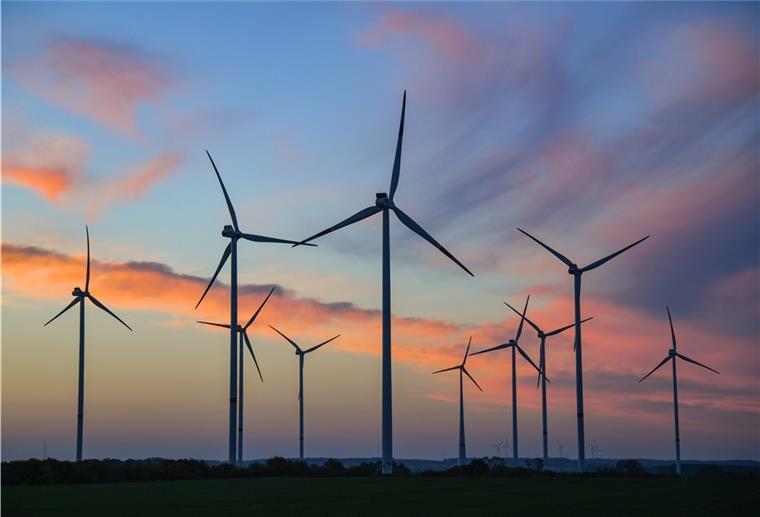 Farbenprächtig leuchten Wolken am Morgenhimmel kurz vor Sonnenaufgang über einem Windpark