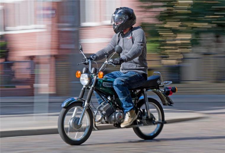 ein junger Mann mit Helm fährt auf einem Mofa