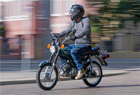ein junger Mann mit Helm fährt auf einem Mofa