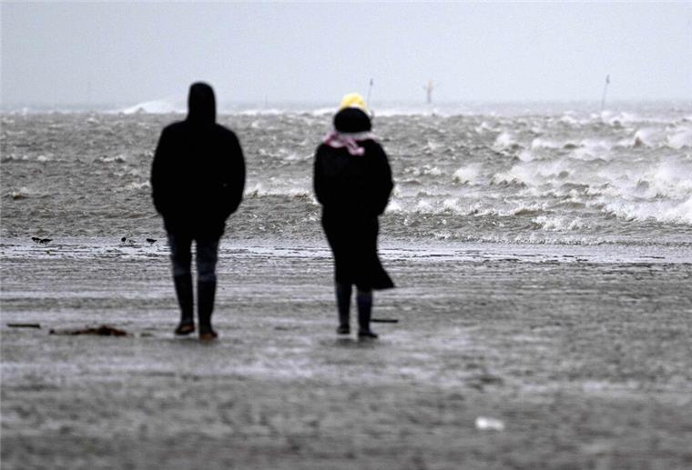 Spaziergänger gehen bei stürmischem Wetter durch das Watt vor dem Strand von Cuxhaven.