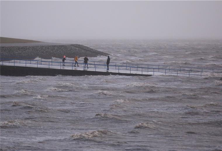 Spaziergänger sind bei Sturm und Einbruch der Dunkelheit an der aufgewühlten Nordsee unterwegs. 