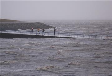 Spaziergänger sind bei Sturm und Einbruch der Dunkelheit an der aufgewühlten Nordsee unterwegs. 