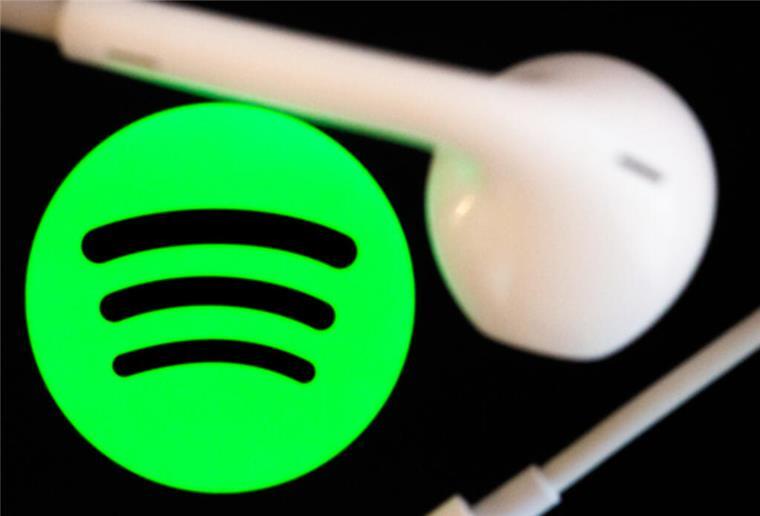 Spotify erweitert das Hörbuchangebot mit 350.000 neuen Titeln Kopfhörer liegen auf dem Bildschirm eines Smartphones, auf dem das Logo vom Musikstreaming-Dienst Spotify angezeigt wird.